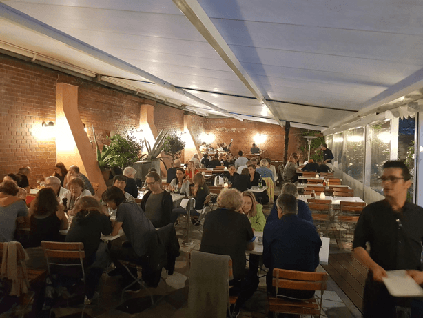 Der Wintergarten der Osteria N.1 mit Backsteinwänden, warmem Licht und besetzten Tischen
